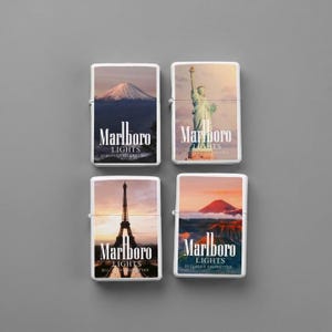 Puede incluir: Cuatro encendedores met&aacute;licos rectangulares con im&aacute;genes impresas del monte Fuji, la Estatua de la Libertad, la Torre Eiffel y un paisaje volc&aacute;nico. Cada encendedor muestra el texto blanco Marlboro LIGHTS y 20 CLASS A CIGARETTES.