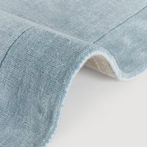 Könnte beinhalten: Ein hellblauer Teppich mit einer dichten, kurzflorigen Textur. Der Teppich ist umgeschlagen und gibt den Blick auf ein helles, gewebtes Trägermaterial frei. Die Oberfläche wirkt gleichmäßig und weich mit subtilen Farbnuancen im blauen Gewebe.