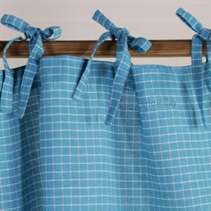 May include: Light blue and white checked curtains with tie fastenings. The curtains feature a grid pattern. The tie fastenings are made from the same fabric and are tied into bows. The word "LOOMOIRE" is printed on the curtain.