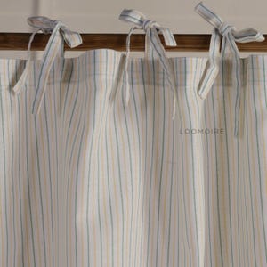 Puede incluir: Cortinas color crema con rayas verticales en amarillo pálido y verde. Las cortinas están atadas con lazos de tela a juego. La palabra "LOOMOIRE" está impresa en la tela de la cortina.