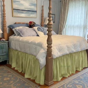 Peut inclure: Un lit à baldaquin en bois avec une couette blanche matelassée et un cache-sommier à rayures vert clair et blanc. Le lit présente plusieurs oreillers dans des tons de bleu et de blanc, dont un oreiller en forme de cœur, sur un mur bleu clair.