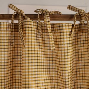 May include: A yellow and white checkered curtain featuring thin black grid lines and fabric tie-top closures draped over a wooden rod. The fabric displays a subtle woven texture throughout, and the word LOOMAIRE is printed in small letters on the right.