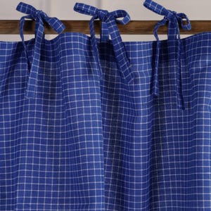 May include: Blue and white checkered curtains with tie-top closures. The curtains are made of a fabric with a grid pattern, and are hanging from a wooden rod. The tie-top closures are made of the same blue fabric.
