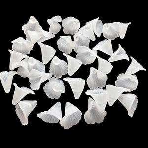 May include: A collection of small, translucent white flower-shaped beads. The beads have a delicate, petal-like design and are scattered against a black background. These beads are ideal for jewelry making or craft projects.