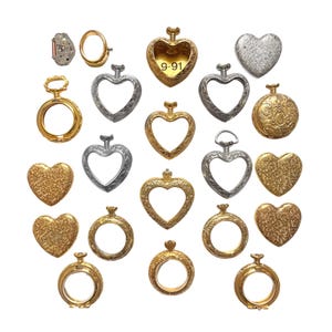 May include: A collection of metal watch components including heart-shaped frames, circular frames, and solid heart-shaped covers in gold and silver tones. One gold heart frame features the engraved text 9-91. Various pieces show intricate textured patterns.