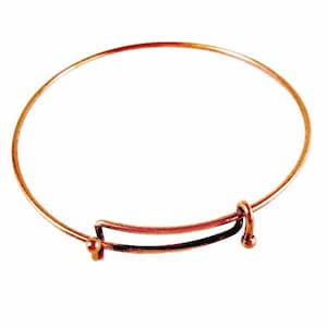 May include: A copper-colored adjustable bangle bracelet. The bracelet features a circular design with an adjustable mechanism. The adjustable section is a rectangular shape with a small ball on each end. The bracelet is designed to be worn on the wrist.