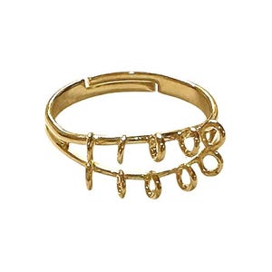 May include: A gold-colored adjustable ring with a unique design. The ring features two parallel bands connected by vertical bars and decorative loops. The ring is set against a white background.