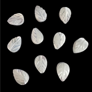 May include: A collection of ten pearly white leaf-shaped beads. Each bead is carved with detailed leaf vein patterns. The beads are arranged against a black background, highlighting their delicate design and texture. Ideal for jewelry making.