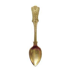 May include: A gold-colored spoon with an ornate handle featuring a floral design. The spoon's bowl is oval-shaped, and the handle has a decorative, detailed pattern. The spoon is likely vintage or antique, and is set against a white background.