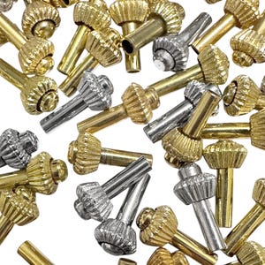 Peut inclure: Un ensemble de petits composants métalliques décoratifs de tons or et argent. Chaque composant présente une tête texturée et détaillée et une tige cylindrique. Les composants sont dispersés sur un fond blanc, créant un arrangement visuellement attrayant.
