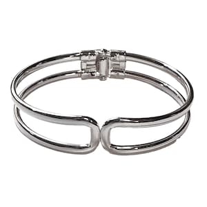 May include: A silver-colored bangle bracelet with a double-band design. The bracelet features a hinged clasp for easy wear and removal. The polished metal reflects light, creating a bright and elegant appearance. This jewelry item is suitable for everyday wear or special occasions.