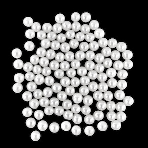 May include: A collection of small, round, white pearls against a black background. The pearls are clustered together, creating a dense, textured appearance. The pearls are evenly sized and have a glossy finish.