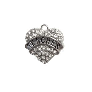 May include: A silver-toned heart-shaped charm with the word "TEACHER" on a banner across the center. The heart is encrusted with clear, sparkling crystals. A small loop is at the top for attachment.