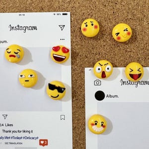 May include: A set of nine yellow emoji magnets with different expressions, such as crying, smiling with hearts, and wearing sunglasses. The magnets are arranged on white Instagram-style paper cutouts.