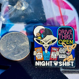 May include: A square enamel pin featuring a grey alien wearing a black cap, holding packets labeled HOT CLOSERS ROCK, FIRE OWN THE NIGHT, and DIABLO 4TH MEAL. Text reads DRIVE THRU OPEN and NIGHT SHIFT. A US quarter is shown for scale next to the pin.