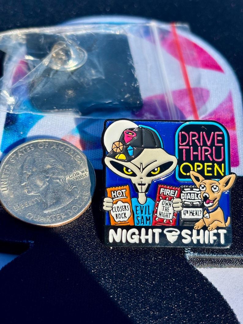 May include: A square enamel pin featuring a grey alien wearing a black cap, holding packets labeled HOT CLOSERS ROCK, FIRE OWN THE NIGHT, and DIABLO 4TH MEAL. Text reads DRIVE THRU OPEN and NIGHT SHIFT. A US quarter is shown for scale next to the pin.
