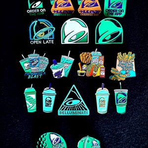 May include: A collection of Taco Bell themed enamel pins featuring various designs including the bell logo, Baja Blast drinks, food boxes, and text such as Order on the App, Open Late, I'm Having a Blast, Belluminati, Golf Mas, and Live Mas.