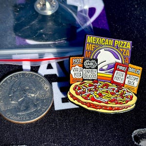 May include: A metal enamel pin featuring a Mexican pizza graphic with four sauce packets labeled Hot, Diablo, Fire, and Mild. The pin includes text reading Mexican Pizza, Viva La Pizza, Sinfully Delicious, Pizza Party, and Welcome Back, next to a US quarter.