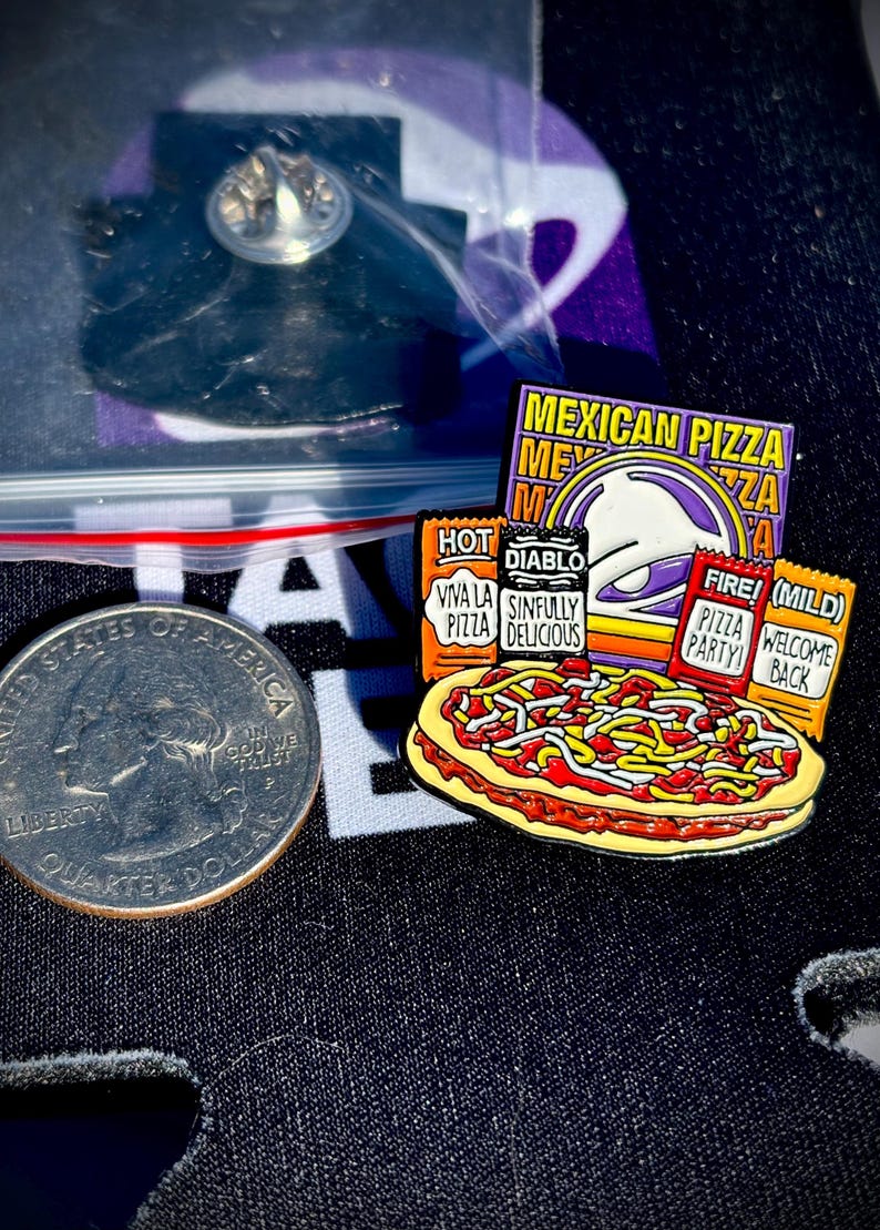 May include: A metal enamel pin featuring a Mexican pizza graphic with four sauce packets labeled Hot, Diablo, Fire, and Mild. The pin includes text reading Mexican Pizza, Viva La Pizza, Sinfully Delicious, Pizza Party, and Welcome Back, next to a US quarter.