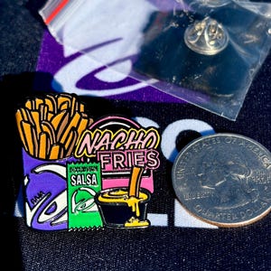 May include: A metal enamel pin featuring a purple container of golden brown fries, a green packet labeled Salsa, and a black cup of yellow cheese sauce with a fry dipped in it. The text Nacho Fries is in pink. A US quarter is shown for scale.