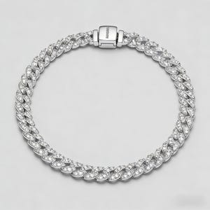 May include: A silver-toned bracelet with a cuban link design. The links are encrusted with clear, sparkling gemstones. The clasp is rectangular and features the brand name. The bracelet is displayed on a light gray background.