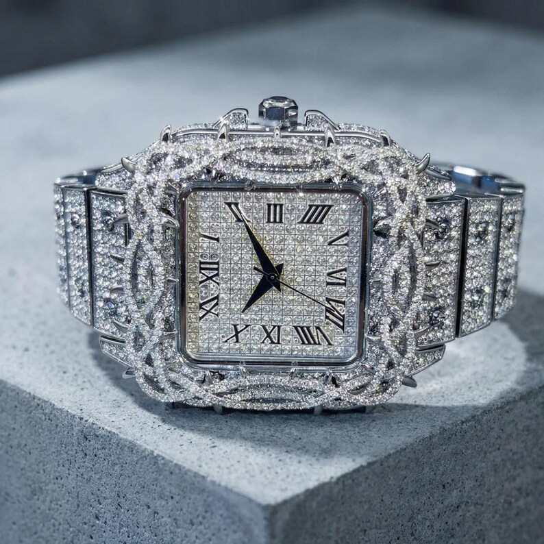 Op de afbeelding: Een luxe horloge met een vierkante wijzerplaat en een zilveren band. Het horloge is bezet met talrijke kleine, sprankelende diamanten. Romeinse cijfers markeren de uren op de wijzerplaat. Het horloge ligt op een grijze ondergrond.