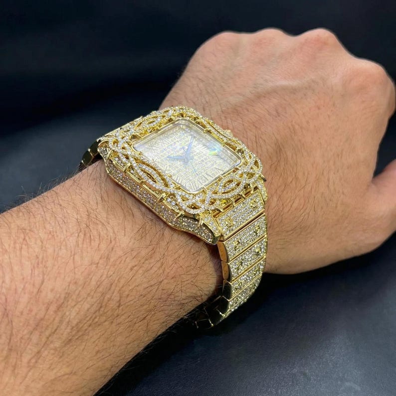 Op de afbeelding: Een goudkleurig horloge met een rechthoekige wijzerplaat en een met diamanten bezette lunette en band. Het horloge heeft een getextureerde wijzerplaat en wordt om de pols bevestigd. Het horloge is een luxe artikel.