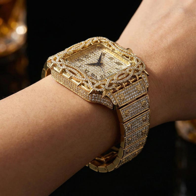 Op de afbeelding: Een goudkleurig polshorloge met een vierkante wijzerplaat en een met diamanten bezette lunette. Het horloge heeft Romeinse cijfers en een bijpassende, met diamanten ingelegde band. Het is een luxe artikel.