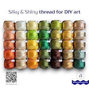 May include: A collection of thirty small, round spools of silky, shiny thread arranged in a grid. Each spool is labeled with a unique numerical code. The text at the top reads Silky & Shiny thread for DIY art. A QR code and a logo are visible.