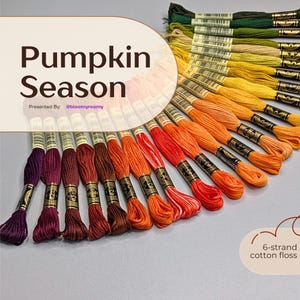 Peut inclure: Une collection d'échevettes de fil à broder en coton à 6 brins disposées en éventail, passant du violet foncé et marron à l'orange vif, au jaune et au vert. Le texte "Pumpkin Season" et "6-strand cotton floss" sont visibles.