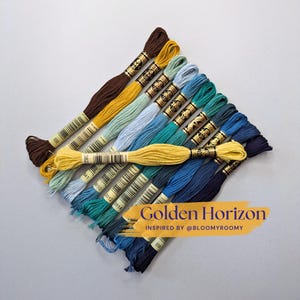May include: A collection of embroidery floss skeins in a gradient of colors ranging from dark brown and yellow to light blue, teal, and deep navy blue. Each skein features a paper label with a barcode. Text reads Golden Horizon INSPIRED BY @BLOOMYROOMY.