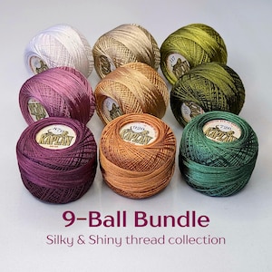 May include: A collection of nine balls of shiny thread in various colors including white, gold, olive green, dark green, copper, and shades of purple. Each ball features a central label with the brand name Kaplan and a specific color number.