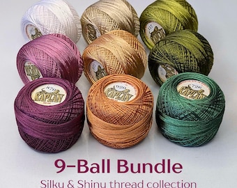 May include: A collection of nine balls of shiny thread in various colors including white, gold, olive green, dark green, copper, and shades of purple. Each ball features a central label with the brand name Kaplan and a specific color number.