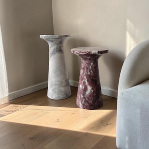Puede incluir: Dos mesas de pedestal cil&iacute;ndricas con tapas acampanadas. Una mesa presenta un patr&oacute;n de piedra veteada en blanco y gris, mientras que la otra muestra un acabado de piedra veteada en color burdeos intenso y blanco. Superficie lisa y pulida.