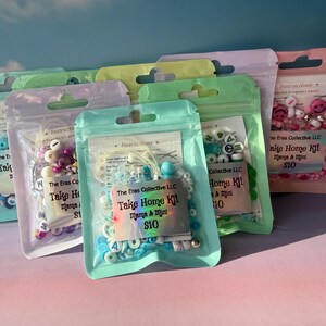 May include: Several colorful plastic zip bags filled with beads and craft supplies. Each bag has a label that reads "Take Home Kit" and includes the text "Mama & Mini". The bags are in various colors, including pink, green, and blue.