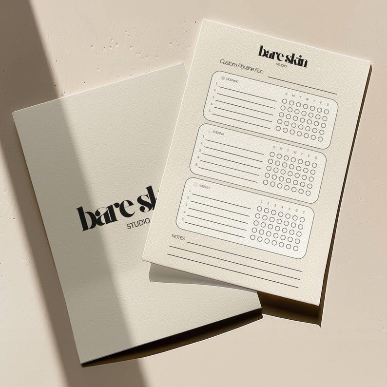 Peut inclure: Deux carnets blanc cass&eacute;. L'un des carnets est ouvert, r&eacute;v&eacute;lant un planificateur de routine personnalis&eacute; avec des sections pour les routines du matin, du soir et hebdomadaires. Le texte "bare skin studio" est imprim&eacute; sur la couverture et le planificateur.