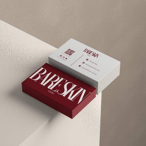 May include: A stack of business cards with the text "BARESKIN STUDIO" in white on a deep red card. A second stack of cards is white with the same text in a burgundy color. The cards have a textured finish and a minimalist design.