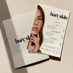 以下が含まれることがあります： モダンなフォントで「bare skin STUDIO」と書かれたクリーム色のパンフレット。パンフレットは開かれており、女性の顔とフェイシャルと高度なトリートメントの価格表が表示されています。
