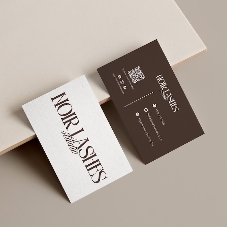 May include: Two business cards with the text "NOIR LASHES Studio" in a serif font. One card is white, the other is dark brown. The brown card includes a QR code, social media icons, and contact information. The cards are on a neutral background.