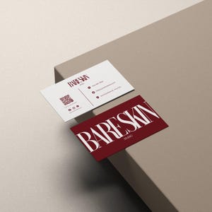 May include: Two business cards with the text "BARESKIN STUDIO". One card is white with burgundy text and a QR code. The other card is burgundy with white text. The cards are on a neutral-toned surface.