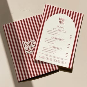 May include: A price menu from Bare Skin Studio, featuring a cream-colored arched top with a list of facials and treatments. The menu is on top of a brochure with a red and white striped pattern. The studio's logo is visible.