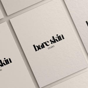 Peut inclure: Plusieurs cartes de visite blanc cass&eacute; avec les mots "bare skin" en gras, en noir. Le mot "STUDIO" est en dessous du texte principal dans une police plus petite. Les cartes sont dispos&eacute;es en biais, cr&eacute;ant une sensation de profondeur et mettant en valeur le design.