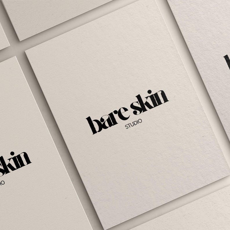 Peut inclure: Plusieurs cartes de visite blanc cass&eacute; avec les mots "bare skin" en gras, en noir. Le mot "STUDIO" est en dessous du texte principal dans une police plus petite. Les cartes sont dispos&eacute;es en biais, cr&eacute;ant une sensation de profondeur et mettant en valeur le design.