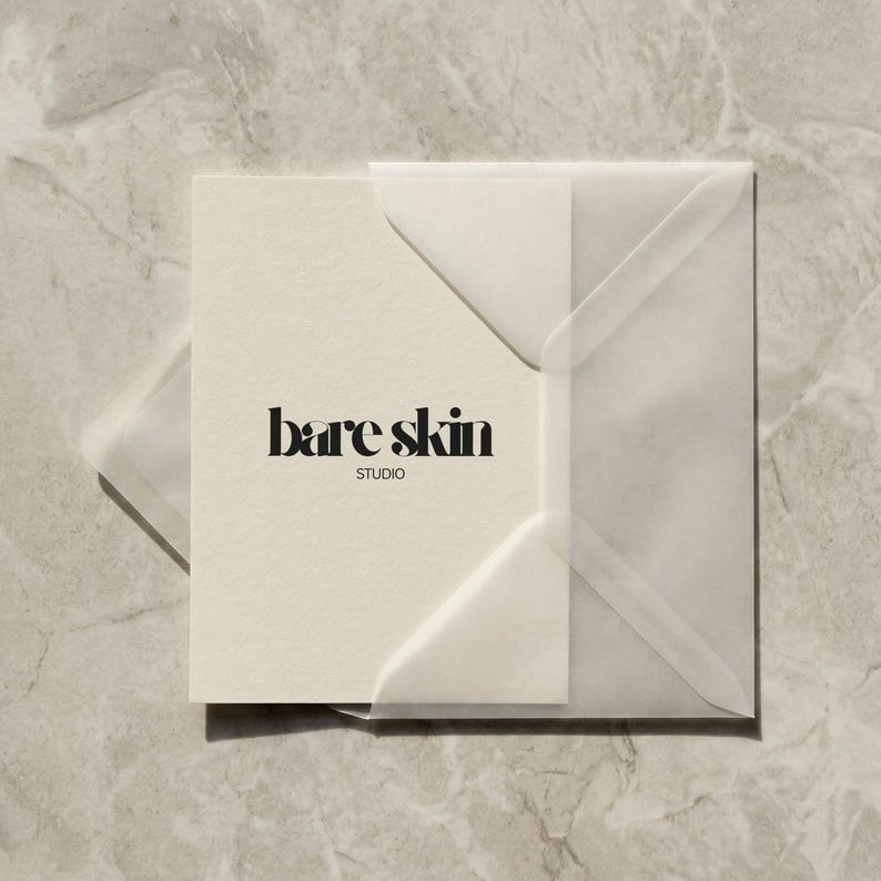Peut inclure: Une carte cr&egrave;me avec le texte "bare skin STUDIO" en noir gras, plac&eacute;e dans une enveloppe translucide. L'enveloppe est carr&eacute;e et poss&egrave;de un rabat. Le fond est un marbre gris clair.