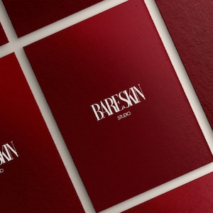Puede incluir: Primer plano de varias tarjetas rectangulares de color rojo oscuro con una superficie texturizada. Las tarjetas presentan el texto blanco "BARESKIN STUDIO" en una fuente estilizada. Las tarjetas est&aacute;n dispuestas en &aacute;ngulo sobre un fondo blanco.