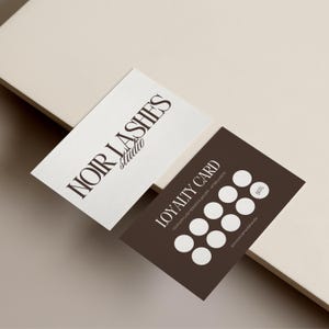 Peut inclure: Deux cartes de visite. Une carte blanche avec "NOIR LASHES studio" en lettres marron foncé. L'autre carte est marron foncé avec les mots "LOYALTY CARD" et plusieurs cercles blancs. La carte contient également le texte "YOUR 6TH LASH SERVICE IS 50% OFF - AFTER 6 VISITS".
