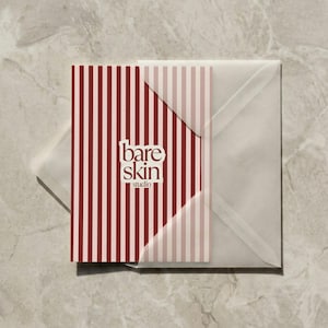 May include: A business card and envelope set. The card features a vertical striped pattern in burgundy and light pink, with the words "bare skin studio" in a white, minimalist font. The envelope is translucent.