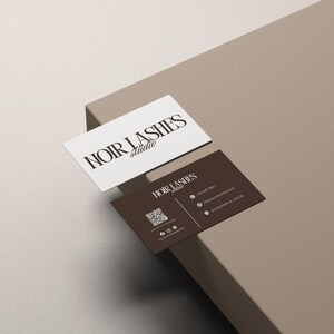 May include: Two business cards with the text "NOIR LASHES studio". One card is white with brown text, the other is brown with white text. The brown card includes a QR code and contact information.