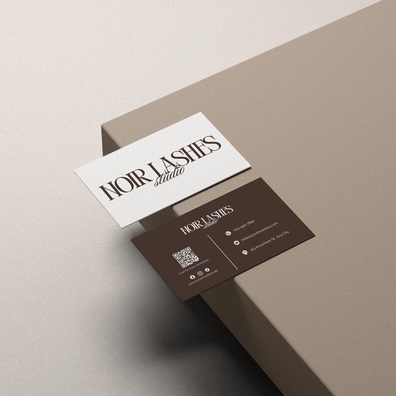 May include: Two business cards with the text "NOIR LASHES studio". One card is white with brown text, the other is brown with white text. The brown card includes a QR code and contact information.