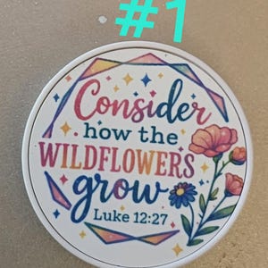 May include: A round, white coaster with the text "Consider how the wildflowers grow" and "Luke 12:27" in colorful script. The design includes floral illustrations and geometric shapes.